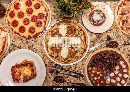 Ensemble de plats de restauration rapide, principalement assortis, pepperoni, fromage et pizzas de tomate, desserts vénézuélien et café sur une surface de granit rouge Banque D'Images