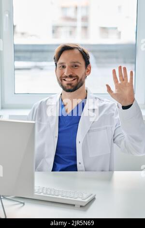 Un médecin sympathique, assis sur son lieu de travail, portant un uniforme médical et se portant la main à l'hôpital Banque D'Images