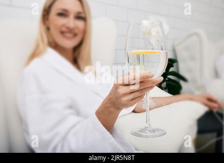 Belle femme avec un verre de boisson rafraîchissante à la chaux pendant le traitement par voie intraveineuse de détox avec perfusion intraveineuse. Soins détox au spa Banque D'Images