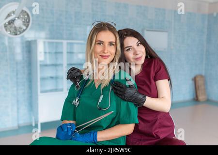 Deux étudiantes ou professionnels de la médecine qui regardent un appareil photo, portant des gommages sur un fond bleu. Banque D'Images