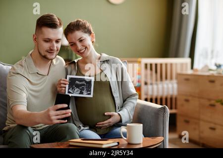 Un jeune couple parle en ligne sur un téléphone portable et partage son bonheur avec des parents qui lui montrent une image échographique Banque D'Images