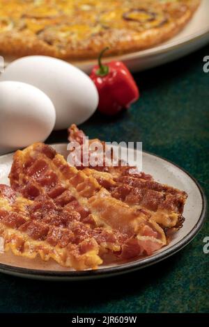 Gros plan de quelques tranches de bacon croustillantes et de trois œufs frais sur le fond. Banque D'Images
