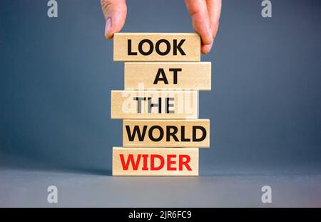 Regardez le symbole du monde entier. Les mots de concept regardent le monde plus large sur des blocs de bois sur un magnifique fond gris. Main d'homme d'affaires. Entreprise et Banque D'Images