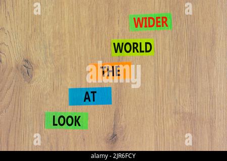 Regardez le symbole du monde entier. Les mots-concepts regardent le monde plus large sur des papiers couleur sur un magnifique fond en bois. Les affaires et le monde Banque D'Images