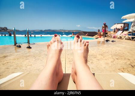 Point de vue de la première personne d'une femme couché sur un transat de piscine donnant sur la piscine avec des personnes en arrière-plan et Copy-sp Banque D'Images