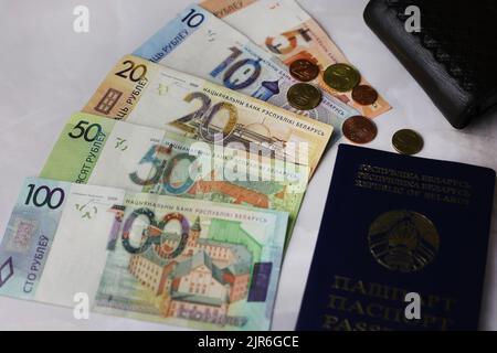 Pièces et billets de 100,50,20,10.5 roubles biélorusses avec un portefeuille noir et un passeport sur fond gris Banque D'Images