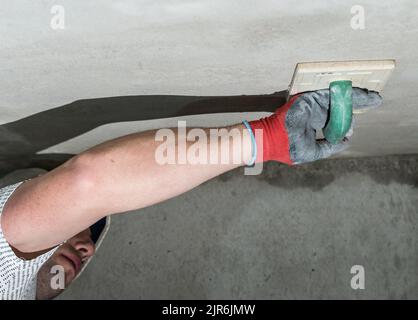 Nivelant le plâtre de chaux avec un râpe avec une éponge absorbant l'humidité, le maître frotte le plafond avec un râpe de construction. Banque D'Images