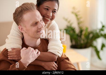 Jeune femme asiatique souriante embrassant son ami heureux de derrière Banque D'Images