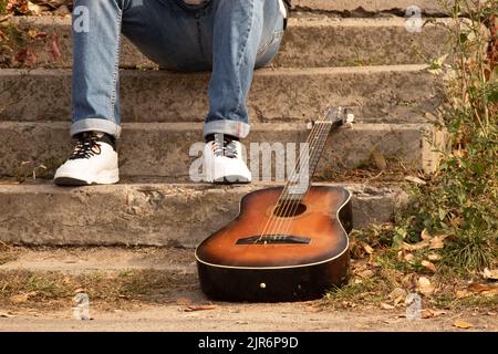 la vieille guitare brune se trouve dans le parc sur les marches près d'un homme en automne au soleil, guitare, passe-temps Banque D'Images