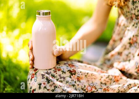 Gros plan d'une bouteille d'eau thermo en acier ECO à la main d'une femme. Fond vert dans le parc. Concept d'espace de copie. Espace pour le texte. Sans plastique. Concept zéro déchet. Mise au point sélective. Banque D'Images