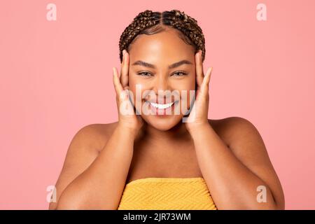 Portrait de la femme afro-américaine touchant le visage sur fond rose Banque D'Images