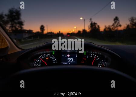 Vue du conducteur sur le compteur de vitesse à 59 km/h ou 59 mi/h, sur une route floue en mouvement, vue de nuit de l'automne depuis l'intérieur d'une voiture du conducteur de la vue du paysage de la route Banque D'Images