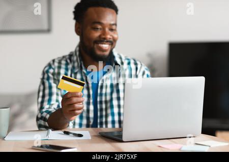 Sourire Black Man Shopping à l'ordinateur portable tenant la carte de crédit à l'intérieur Banque D'Images