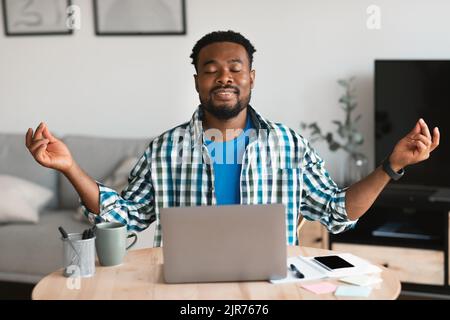 Homme afro-américain détendu méditant sur un ordinateur portable assis sur le lieu de travail Banque D'Images
