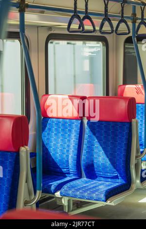 Paire de sièges bleus rouges vides dans une voiture de transport public éclairée par le soleil Banque D'Images