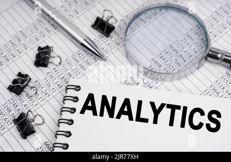 Concept économique et commercial. Sur la table se trouve une loupe, des rapports, un stylo et un bloc-notes avec l'inscription - ANALYTIQUE Banque D'Images