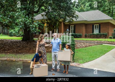 Une mère et un père de famille mélangés et deux jeunes enfants tenant des boîtes d'emballage et se déplaçant dans leur nouvelle maison Banque D'Images