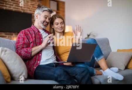 Couple caucasien mûr et souriant, main dans un ordinateur portable, se réunir, assis sur un canapé Banque D'Images