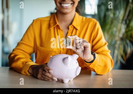 Concept d'épargne, d'investissement, de profit d'entreprise. Femme d'affaires mettant le bitcoin dans la banque de porc rose, assis dans le bureau Banque D'Images