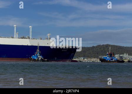 Deux remorqueurs assistent un grand cargo LNG Tanker dans une baie calme avec un ciel dégagé Curtis Island Queensland Australie Banque D'Images