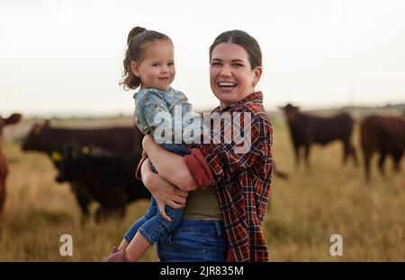 Famille, mère et bébé sur une ferme avec des vaches en arrière-plan mangeant l'herbe, la durabilité et l'agriculture. Bonne maman de producteur de lait biologique avec elle Banque D'Images