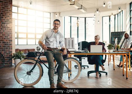 Nous aimons garder les choses décontractées ici. Portrait d'un homme d'affaires mature debout dans un bureau moderne avec son vélo. Banque D'Images