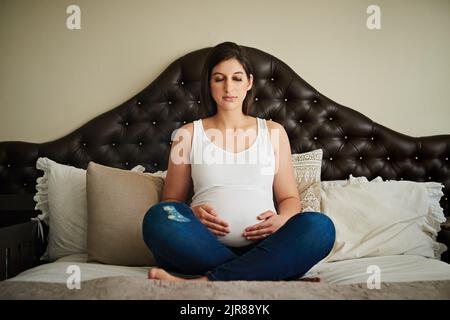 Préparer son esprit pour son arrivée une femme enceinte méditant sur son lit tout en se berlant le ventre. Banque D'Images
