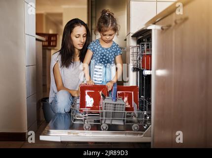 Élever une petite fille responsable. Une petite fille mignonne et sa mère chargeant le lave-vaisselle ensemble à la maison. Banque D'Images