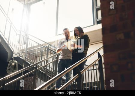 Marchez avec moi... photo sous angle de deux jeunes designers regardant une tablette numérique tout en marchant dans un escalier. Banque D'Images