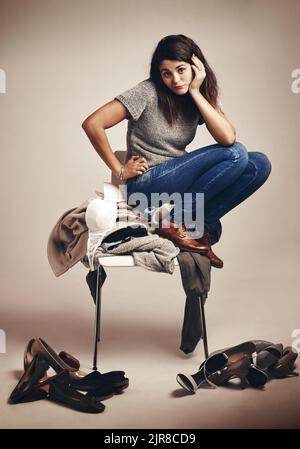 Essayer de trouver la tenue parfaite. La lutte est réelle. Studio photo d'une jeune femme essayant de choisir une tenue d'un tas de vêtements contre un Banque D'Images