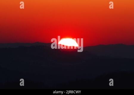 Une vue panoramique d'un soleil rouge partiellement caché derrière les montagnes de la forêt Banque D'Images