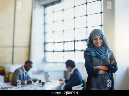 Le succès provient de la bonne mentalité et de la bonne conduite. Portrait d'une femme d'affaires musulmane debout dans un bureau avec ses collègues en arrière-plan. Banque D'Images