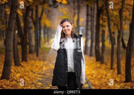 Portrait d'une jeune femme d'Asie centrale dans un parc d'automne sur une ruelle avec des feuilles d'automne tombées Banque D'Images