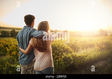 La terre s'étend sur des kilomètres. Un jeune couple qui marche à travers leurs récoltes tout en se tenant les uns les autres et en regardant l'horizon. Banque D'Images