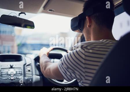 Vous ne vous ennuierez plus jamais dans la circulation. Un jeune homme heureux conduisant une voiture tout en portant un casque de réalité virtuelle. Banque D'Images