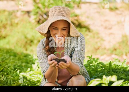 La vie ne cesse jamais de l'émerveiller. Un jeune agriculteur heureux tenant une pile de sol avec une plantule qui en sort. Banque D'Images