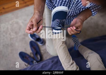 L'aider avec ses lacets. Photo en grand angle d'un homme méconnaissable nouant les lacets de ses fils à la maison. Banque D'Images