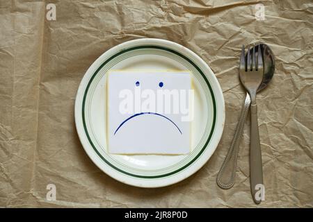 triste udibka dessiné sur un morceau de papier se trouve sur une assiette vide sur la table, tristesse quand il n'y a rien à manger, faim et mauvaise humeur Banque D'Images