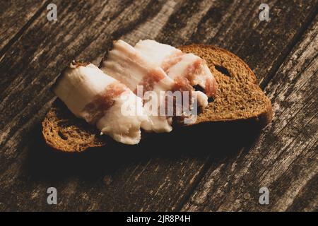 un morceau de pain noir et de tranches de bacon se trouve sur une table en bois, du pain au bacon Banque D'Images