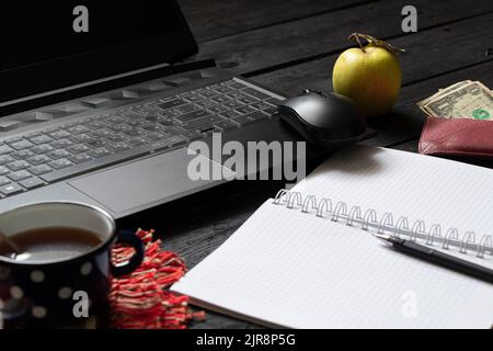 un bloc-notes noir pour ordinateur portable avec de l'argent pour le café se trouve sur la table de travail en bois noir, un ordinateur portable sur la table de travail pendant le travail, processus créatif, indépendant Banque D'Images