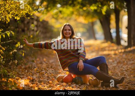 Souriez la femme assise sur la citrouille sur les feuilles d'érable d'autumanl Banque D'Images