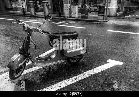 Une photo en niveaux de gris d'un scooter Vespa italien stationné sur la route Banque D'Images