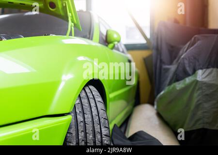 Vue rapprochée de la roue d'un véhicule de course de voiture de sport de rue personnalisé au garage de la station-service avec capot ouvert contre lunette arrière rétroéclairée. Voiture Banque D'Images