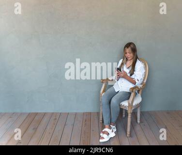 Jeune fille caucasienne avec une peau bronzée et des cheveux justes utilisant des écouteurs sans fil pour appeler un ami via smartphone tenant un téléphone portable. Photo de haute qualité Banque D'Images