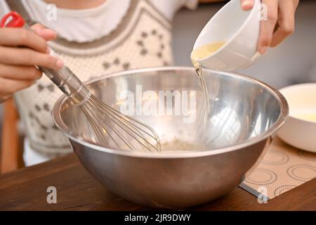 Une femme verse une tasse de blanc d'œuf dans le bol à mélanger avec le mélange de cupcake et le fouetter ensemble. Concept de recette de cupcake. Pantakes et gros plan Banque D'Images