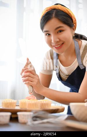 Belle femme faisant le cupcake, décorant le cupcake avec la crème dans la cuisine Banque D'Images