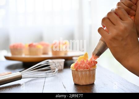 Vue rapprochée de la femme utilisant un sac de crème pour décorer le cupcake, faire le cupcake Banque D'Images