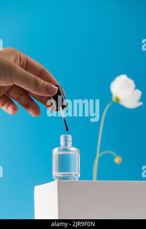 La main d'une femme sort une brosse d'un pot de vernis à ongles médical transparent Banque D'Images