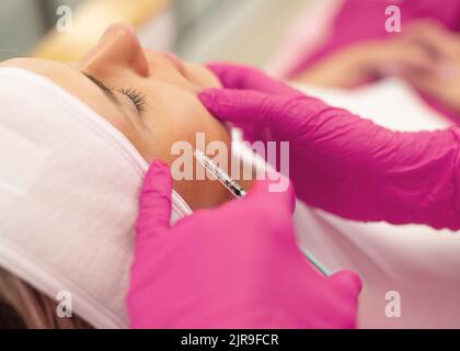 Vue latérale de la jeune femme obtenant rajeunissement injection de collagène dans les pommettes soulevant la peau du visage. Cosmétologie. Banque D'Images