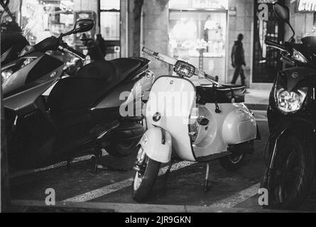Une photo en niveaux de gris d'un scooter Vespa italien stationné à côté d'autres vélos Banque D'Images